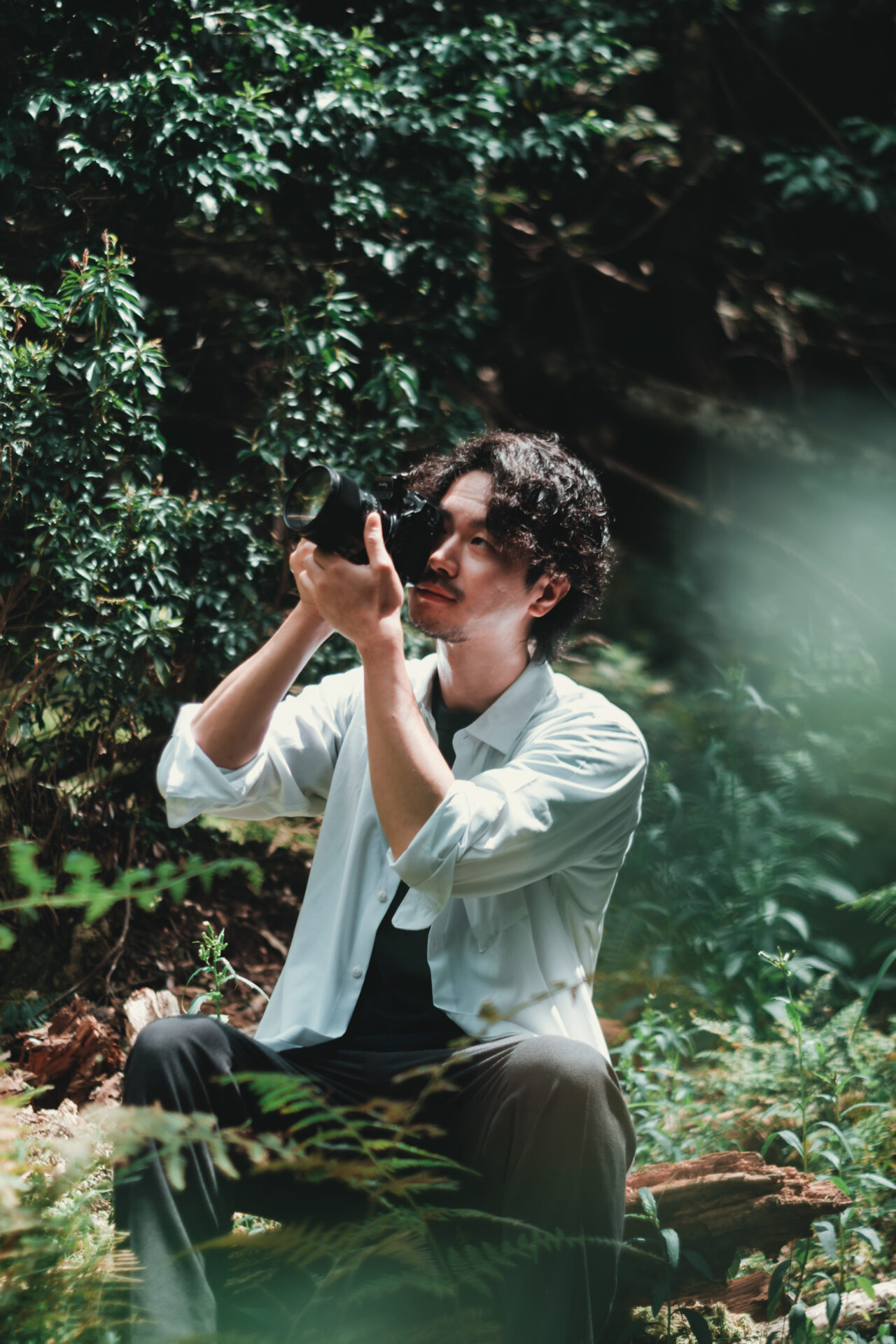 森の中で一眼カメラを構え、被写体を見つめる男性フォトグラファーの姿