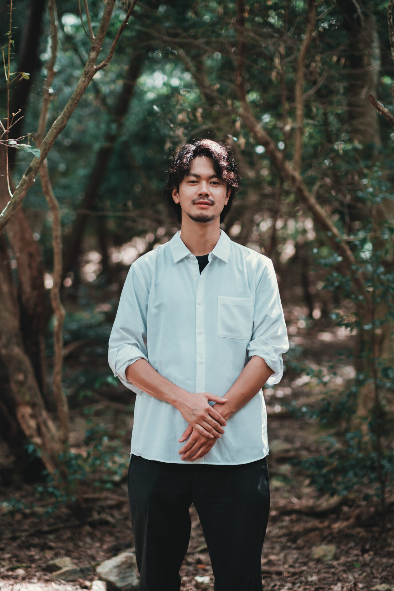 森の中で穏やかな表情で立つ男性フォトグラファーのポートレート写真