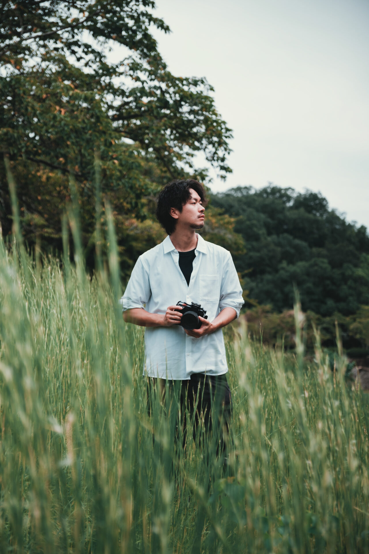 背の高い草原の中でカメラを手に持ち、遠くを見つめる男性フォトグラファーのポートレート