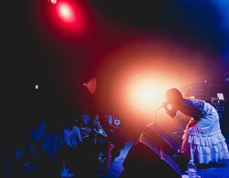 ステージで歌うアーティストを、強いライトが照らすライブシーン。観客と光の中で感情が交錯する瞬間。