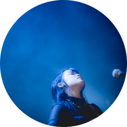 青いライトに照らされながらステージで歌う女性アーティストのライブシーン