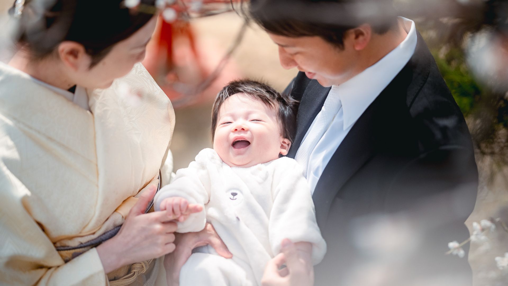 赤ちゃんを抱く両親が笑顔で寄り添い、生まれたばかりの子どもが嬉しそうに笑うファミリーフォト