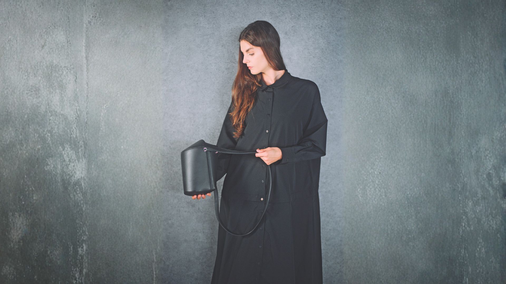 黒いワンピースを着た女性が、デザイン性の高い黒のバッグを手に持って見せるプロダクト撮影シーン