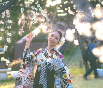 桜の木の下で微笑む女性のポートレート。柔らかな夕陽が着物の柄を照らし、春の温かさを感じる写真。