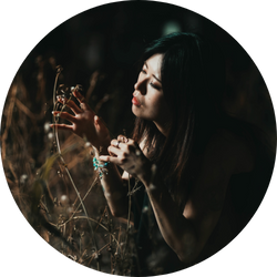 薄暗い草花に触れる女性を捉えたアートスタイルのポートレート写真