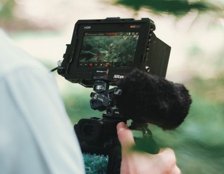 映像用モニターに映る自然の風景を確認しながら撮影するカメラマンの手元。